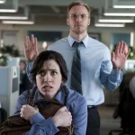 Eine verängstigte Frau in einem Büro, die Anzeichen von Mobbing zeigt, während ein männlicher Kollege im Hintergrund eine abweisende Haltung einnimmt.